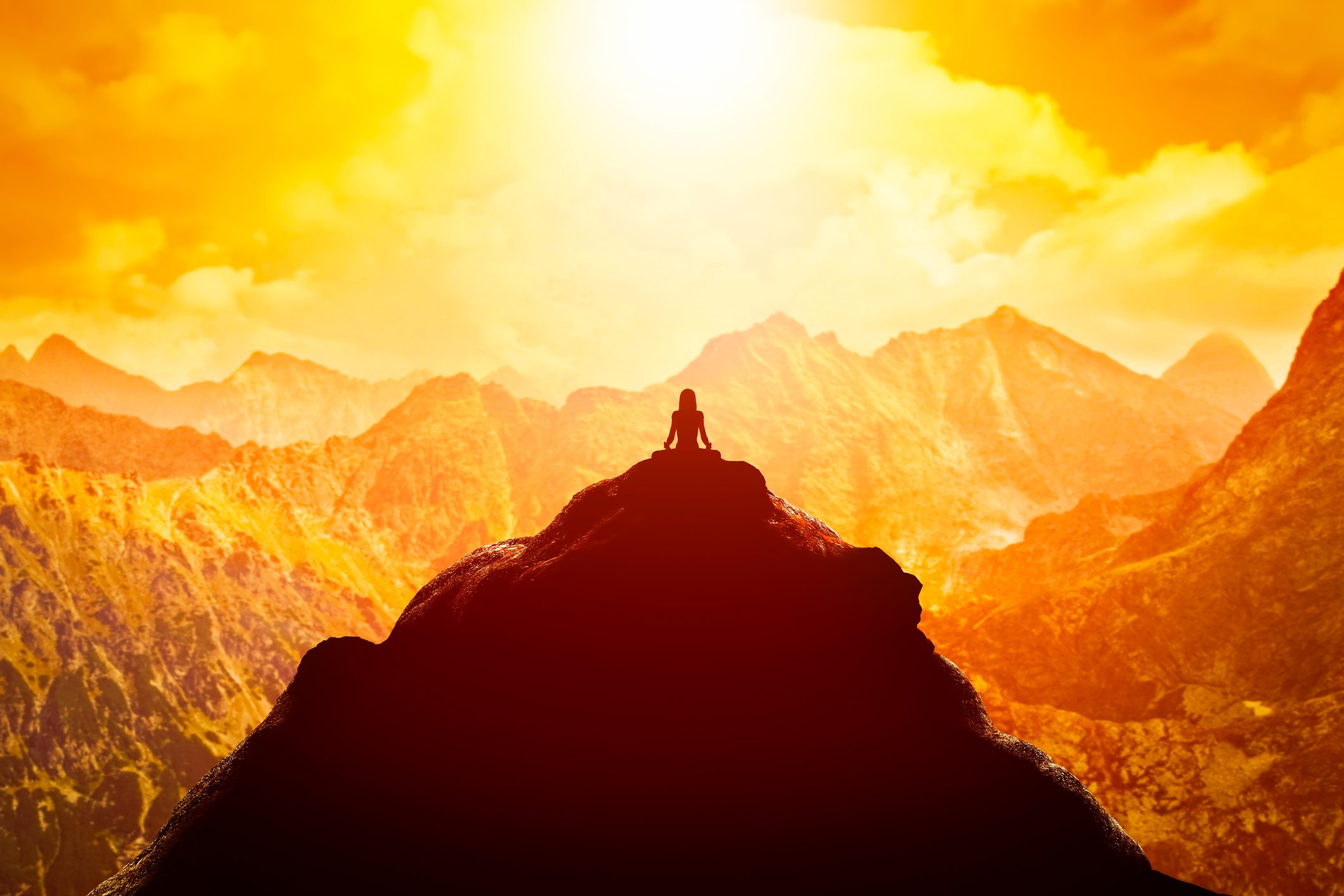 Woman meditating in sitting yoga position on the top of a mountains above clouds at sunset.